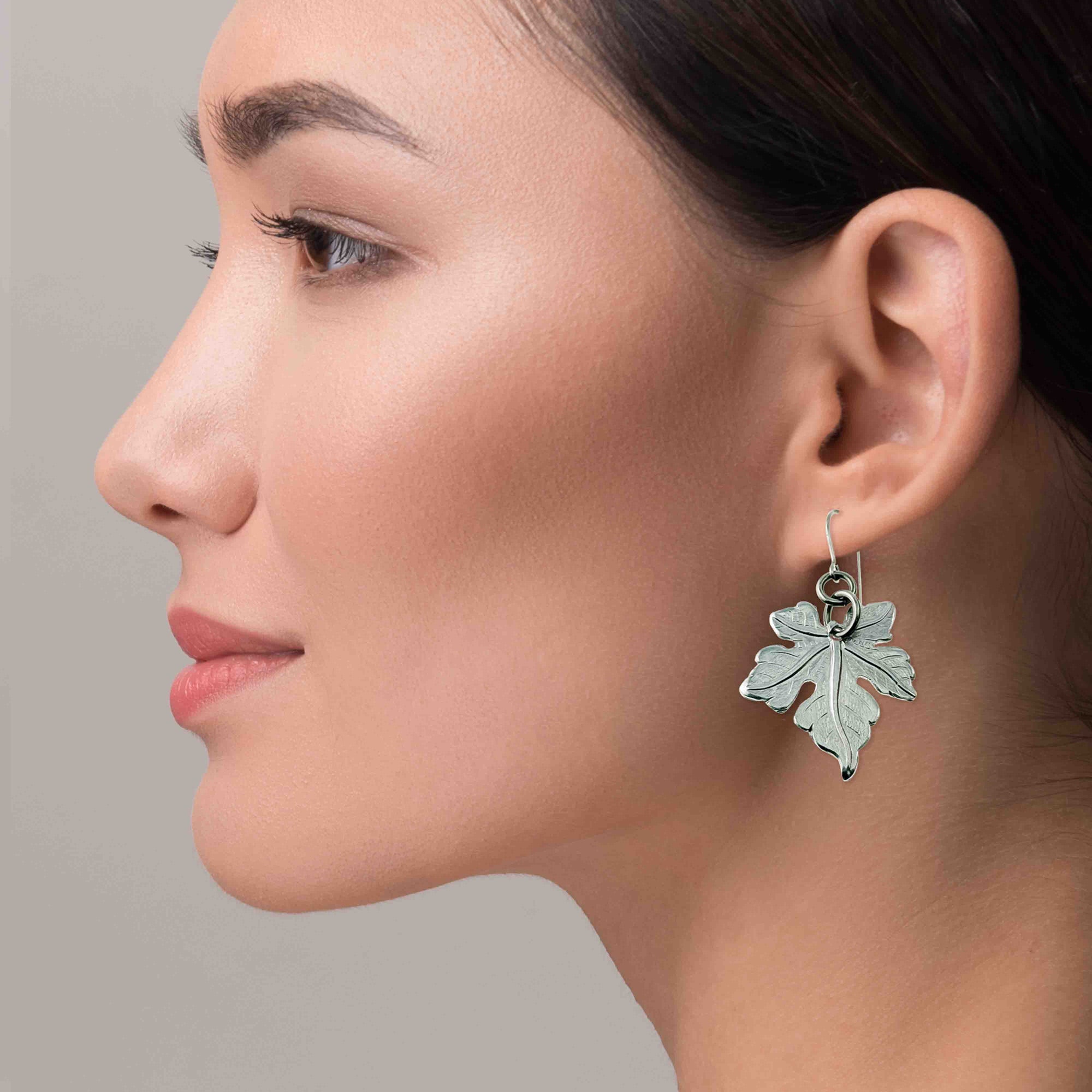 Close-up of a woman wearing a Medium Maple Leaf Aluminum Dangle Earring against a neutral background