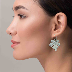 6 of 7: Close-up of a woman wearing a Medium Maple Leaf Aluminum Dangle Earring against a neutral background