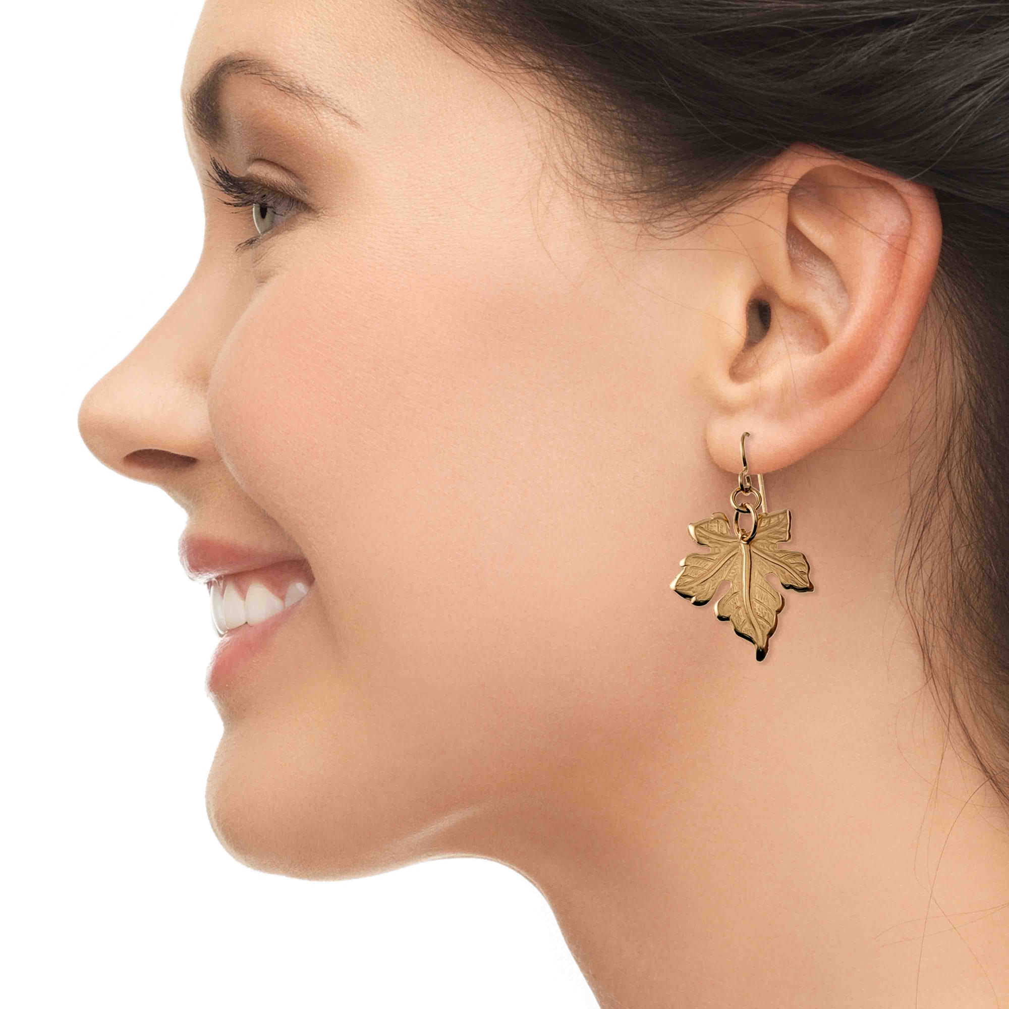 Close-up of a woman wearing a Medium Maple Leaf Bronze Dangle Earring on a white background