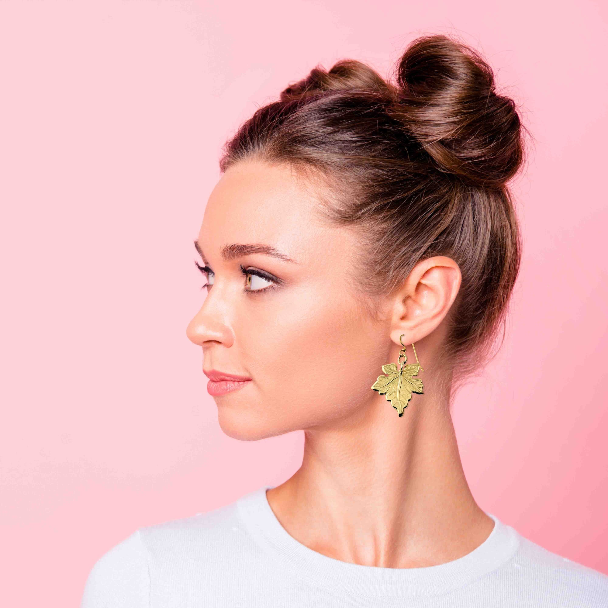 Woman wearing a Medium Maple Leaf Nu Gold Brass Dangle Earring against a pink background