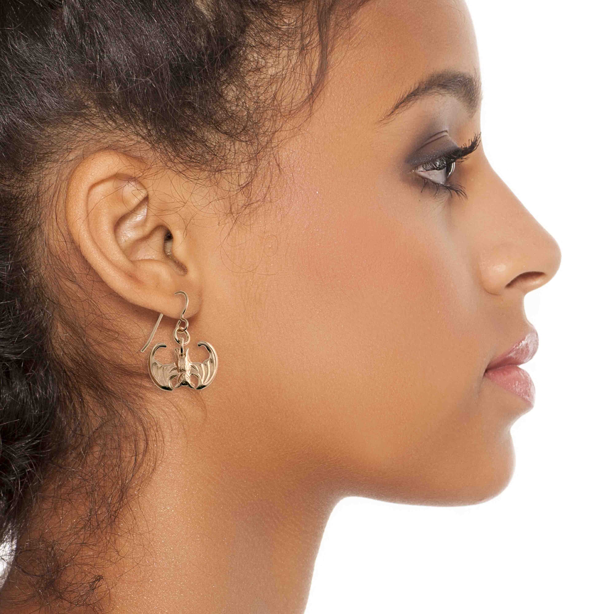 Close-up of a woman wearing Mini Vampire Bat Bronze Dangle Earrings on a white background