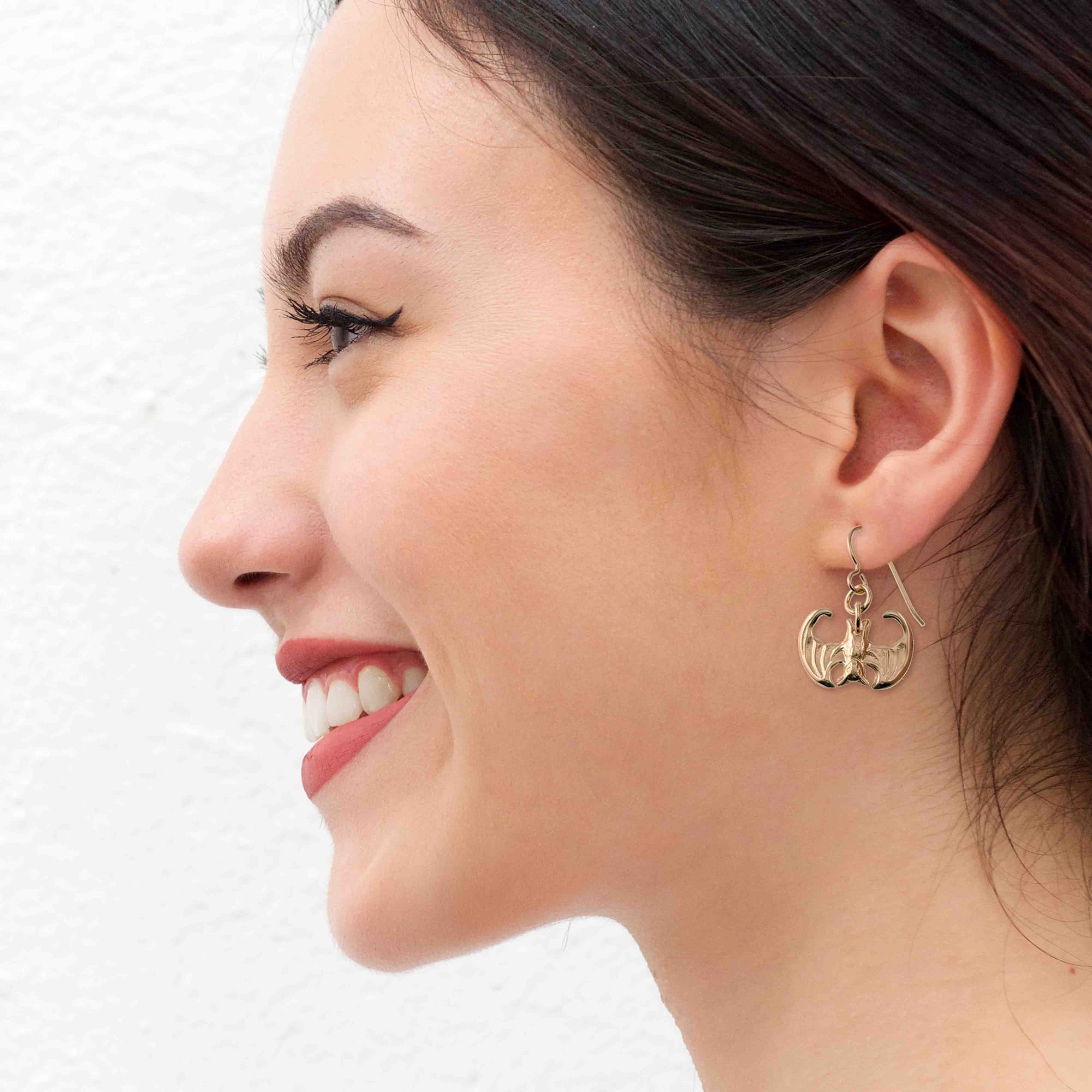 Woman wearing Mini Vampire Bat Bronze Dangle Earrings with a white background