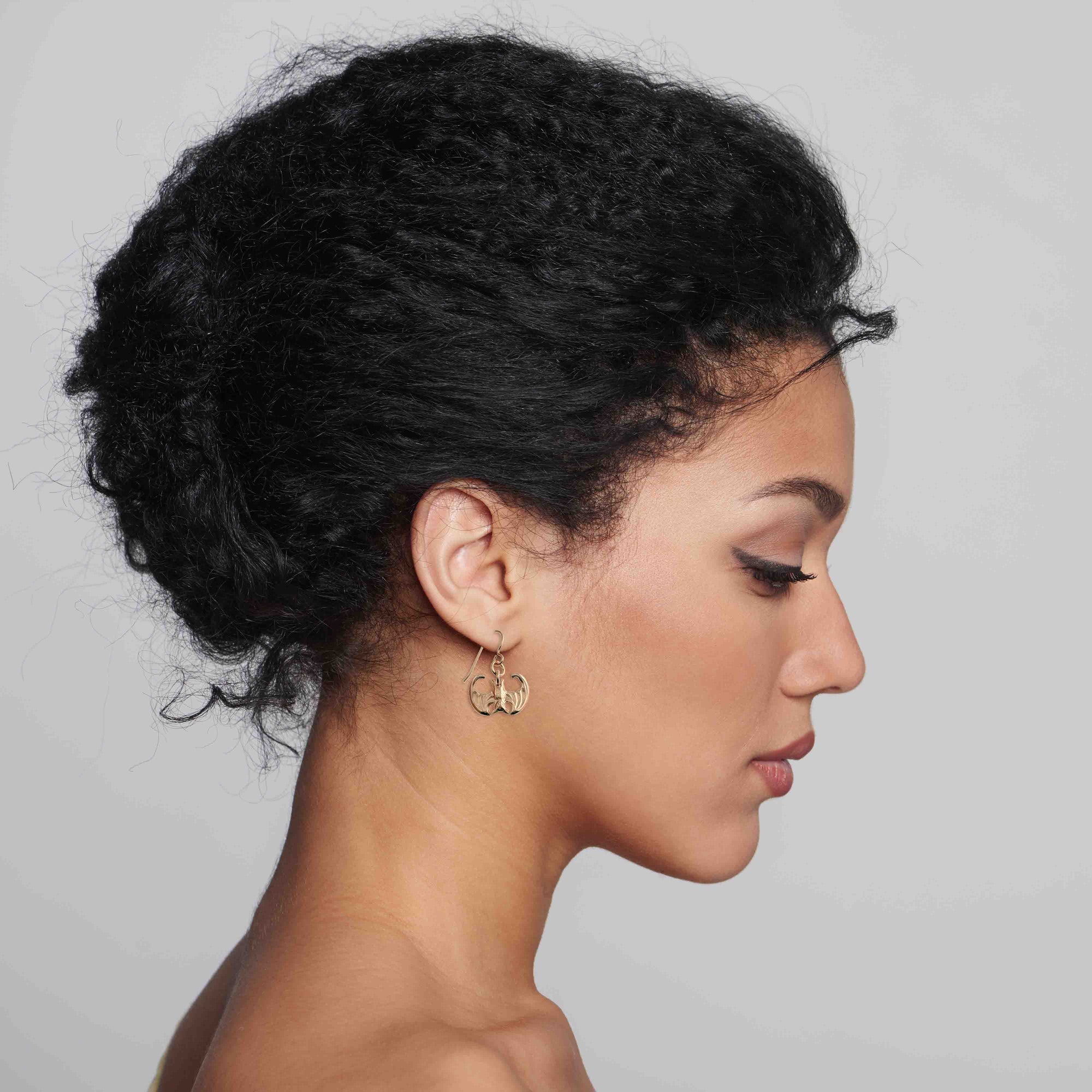 Side profile of a woman with styled hair wearing Mini Vampire Bat Bronze Dangle Earrings against a plain background