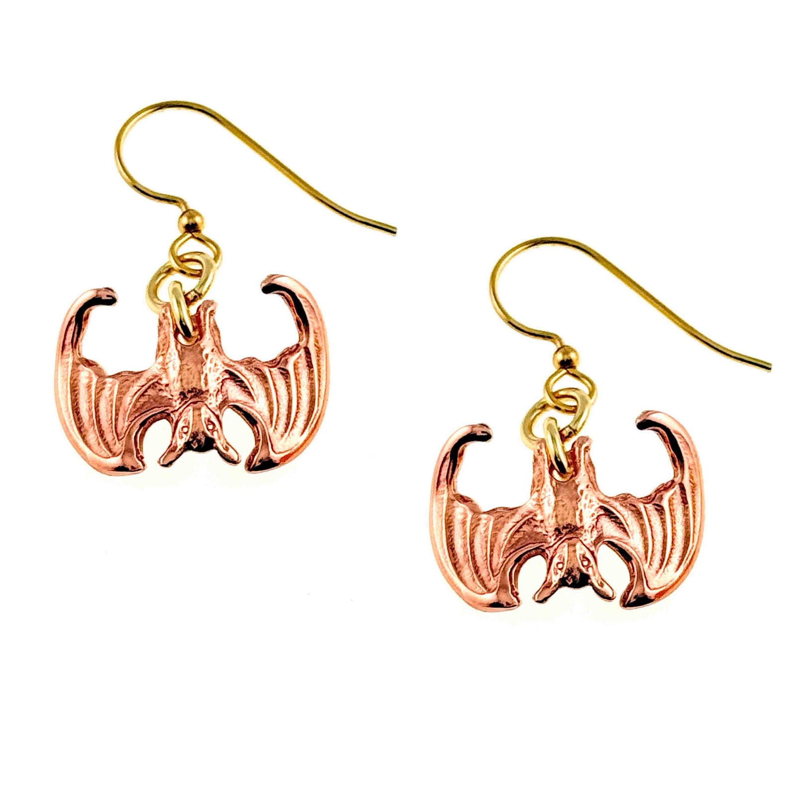 Close-up image of a pair of handcrafted copper dangle earrings shaped like miniature vampire bats with outstretched wings, featuring detailed die-struck textures and hanging from brass French ear wires.