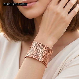 6 of 9: Close view of a woman in a white blouse wearing the Mosaic Embossed Anticlastic Copper Cuff Bracelet. Her raised hand frames the wide bracelet, showing its irregular tile pattern, warm copper color, curved profile, and polished edges. A black label identifies the model as AI generated.