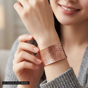 4 of 9: Smiling woman in a gray knit sweater wearing the wide copper cuff near her hand. Her other hand lightly touches the bracelet, drawing attention to the warm brushed finish, dark mosaic lines, and gently flared anticlastic shape. A black label identifies the model as AI generated.