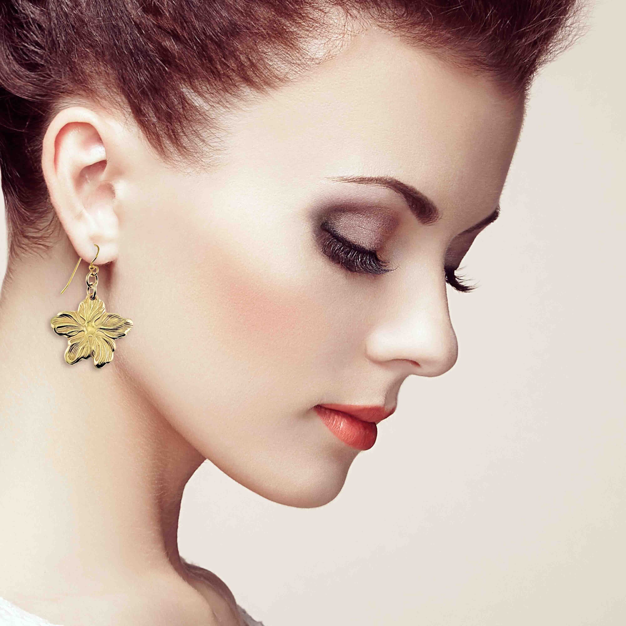 Close-up of a woman wearing Nu Gold Brass Hibiscus Flower Dangle Earrings  with a soft background