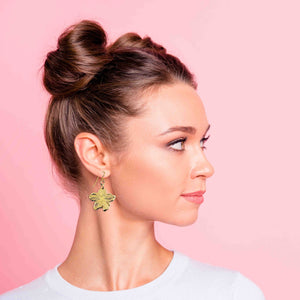 2 of 7: Woman with styled hair wearing Nu Gold Brass Hibiscus Flower Dangle Earrings against a pink background