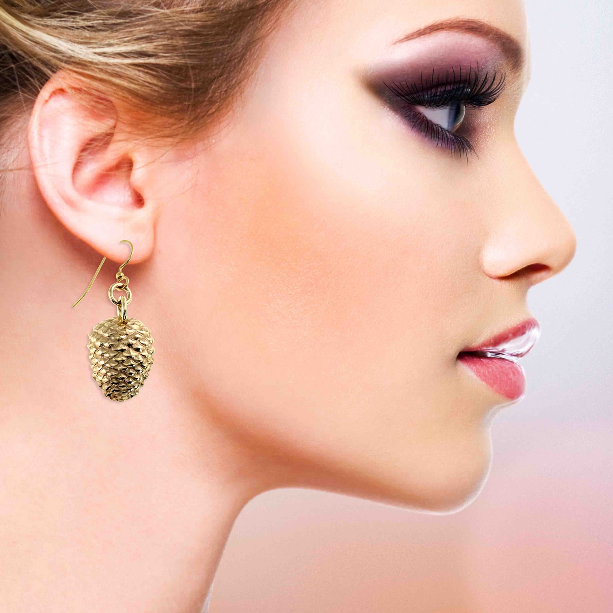 Close-up of a woman's profile wearing Nu Gold Brass Pinecone Dangle Earrings with a soft background