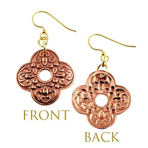 3 of 7: Front and back view of ornate clover-shaped copper drop earrings with detailed scrollwork and a small center cutout. The front shows polished raised patterns, while the back reveals a softer, textured finish. Each earring hangs from gold tone brass French ear wires, displayed on a clean white background with labels indicating front and back.
