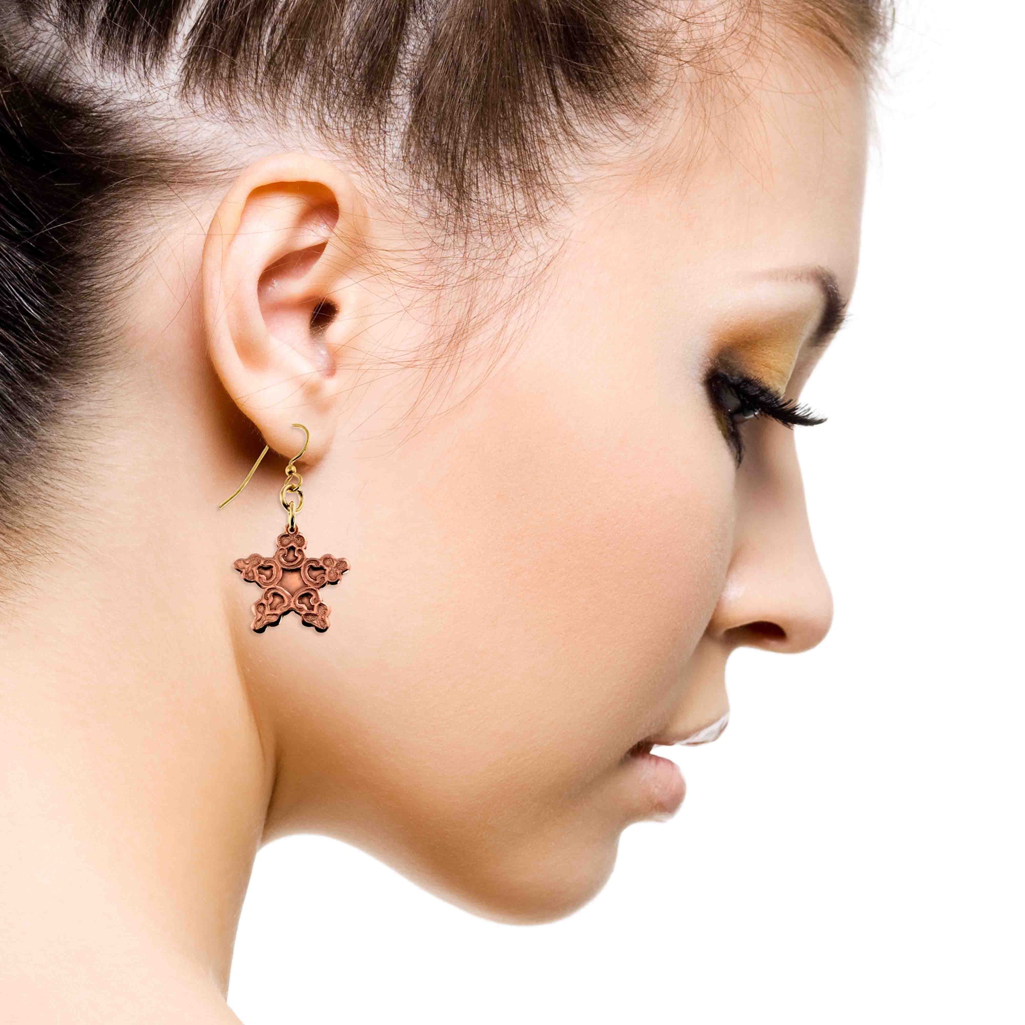 Close-up of a woman's profile wearing a Small Copper Snowflake Dangle Earring on a white background