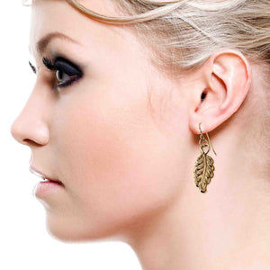 2 of 7: Woman wearing handcrafted Small Feather Bronze Dangle Earrings by John S. Brana, featuring detailed feather design and bronze French hooks.