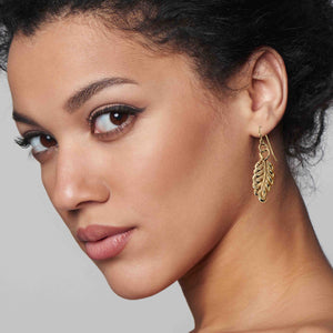 4 of 7: Woman wearing John S. Brana Small Feather Bronze Dangle Earrings, showcasing the detailed die-struck feather design and warm bronze finish.