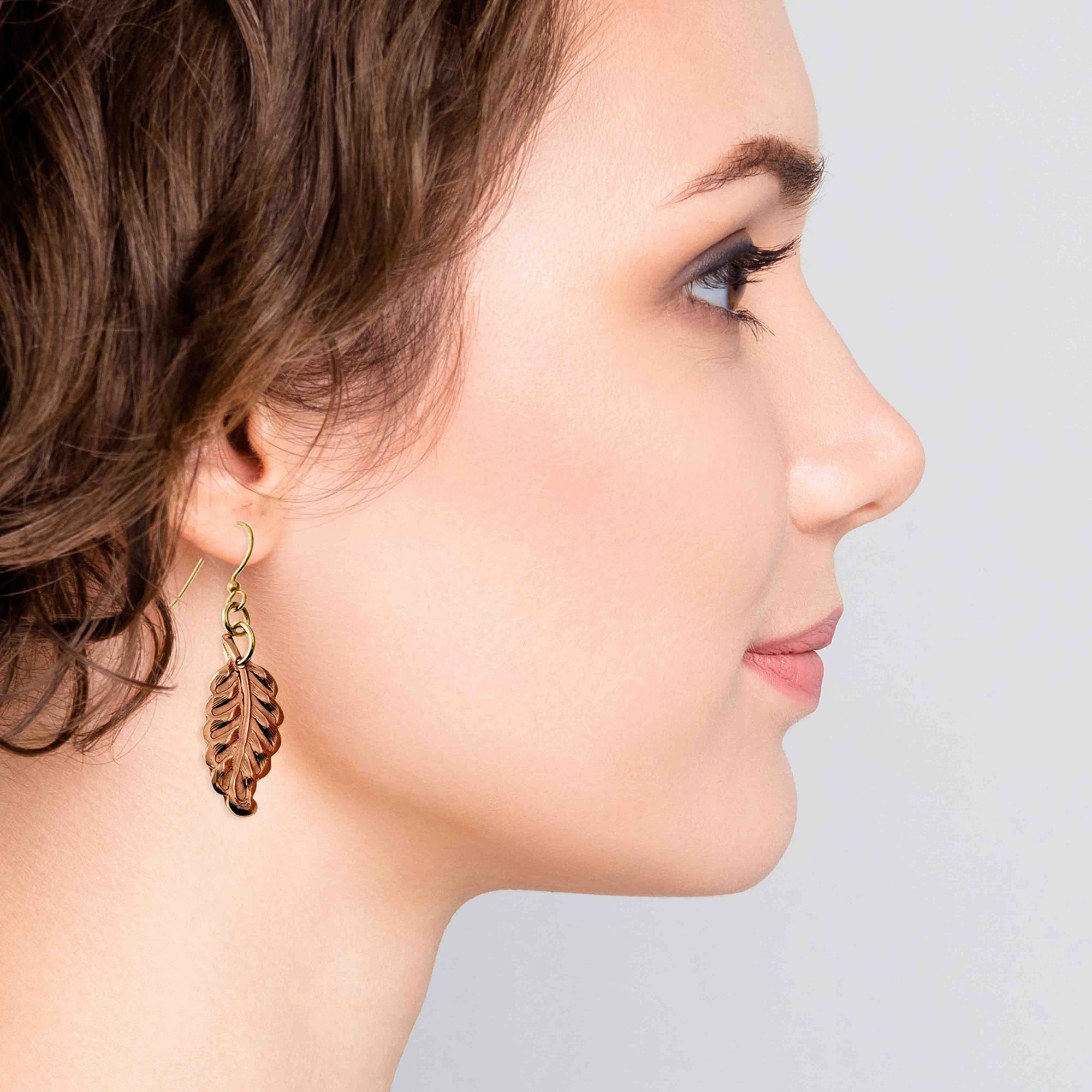 Woman wearing Small Feather Copper Dangle Earrings against a light background