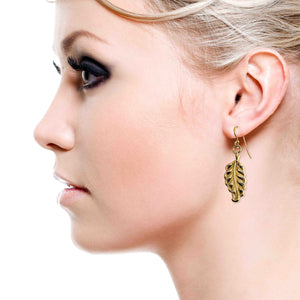 4 of 7: Close-up of a woman wearing a Small Feather Nu Gold Brass Dangle Earring on a white background