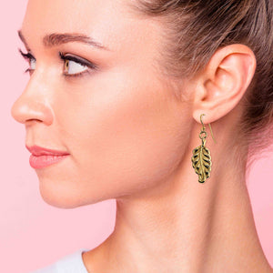 2 of 7: Close-up of a woman wearing Small Feather Nu Gold Brass Dangle Earrings  against a pink background