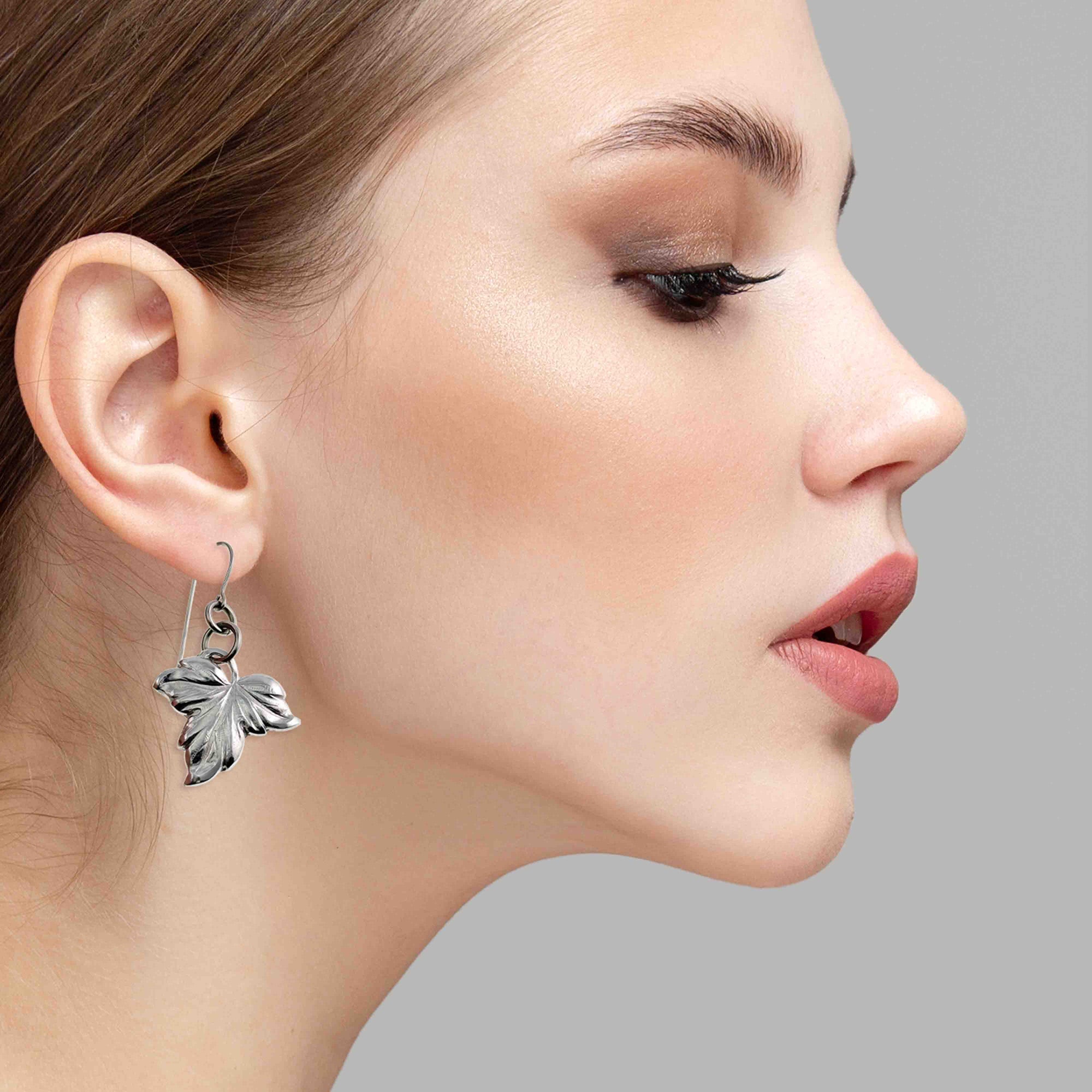 Close-up of a woman wearing Small Maple Leaf Aluminum Dangle Earrings against a neutral background