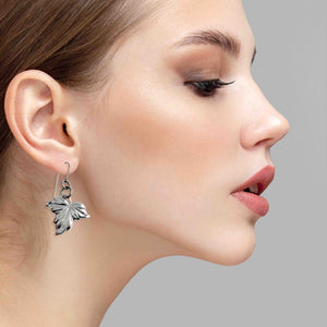 2 of 7: Close-up of a woman wearing Small Maple Leaf Aluminum Dangle Earrings against a neutral background
