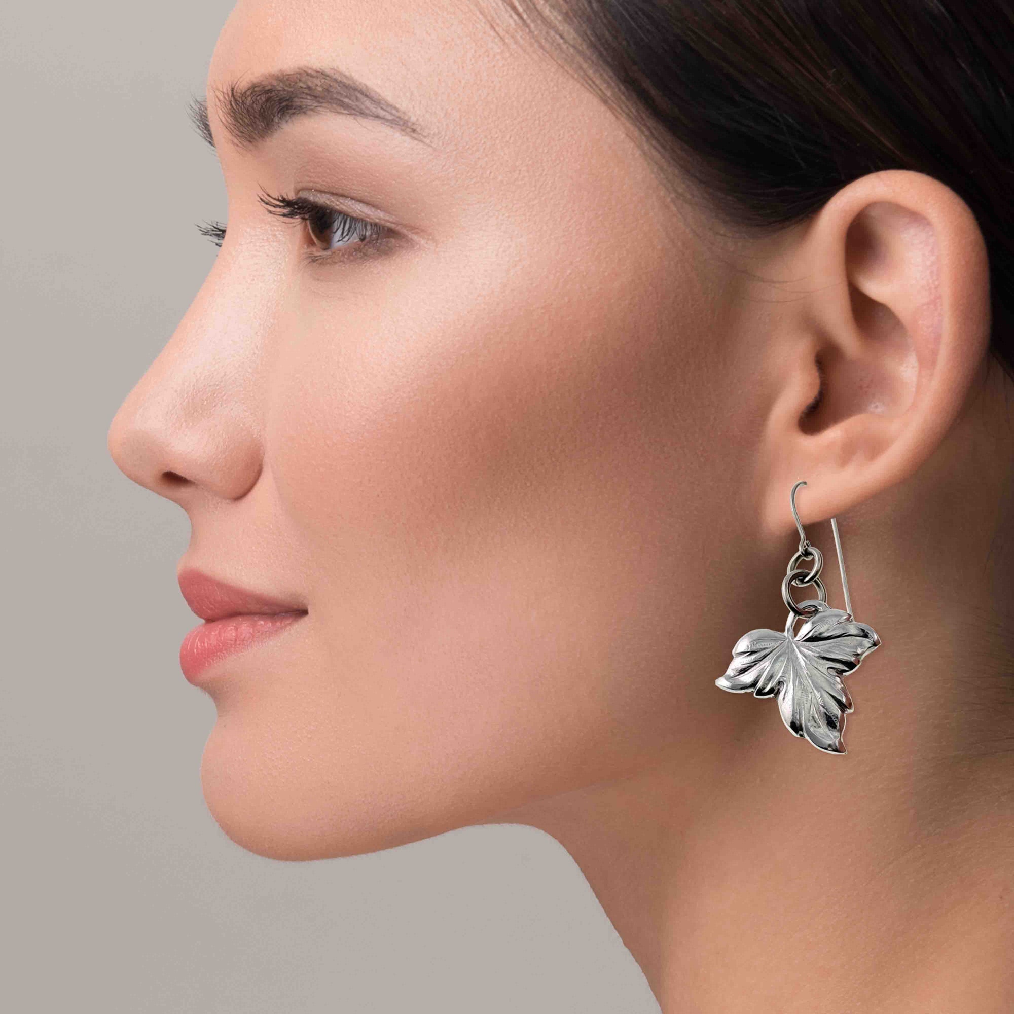 Close-up of a woman wearing Small Maple Leaf Aluminum Dangle Earrings against a neutral background