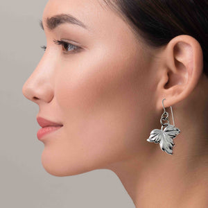 6 of 7: Close-up of a woman wearing Small Maple Leaf Aluminum Dangle Earrings against a neutral background