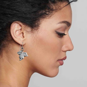 4 of 7: Close-up of a woman wearing a Small Maple Leaf Aluminum Dangle Earring against a neutral background