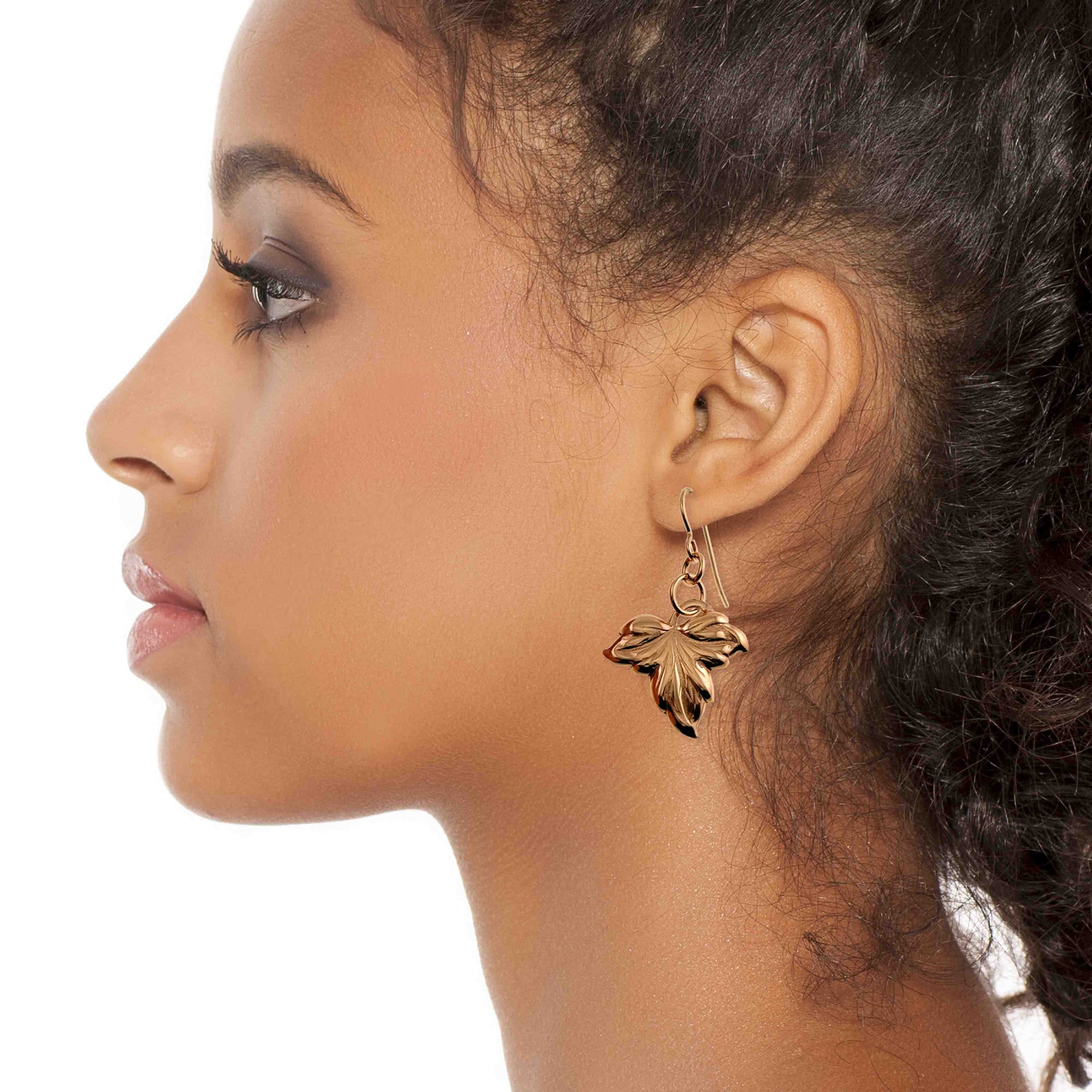 Close-up of a woman wearing a Small Maple Leaf Bronze Dangle Earring on a white background