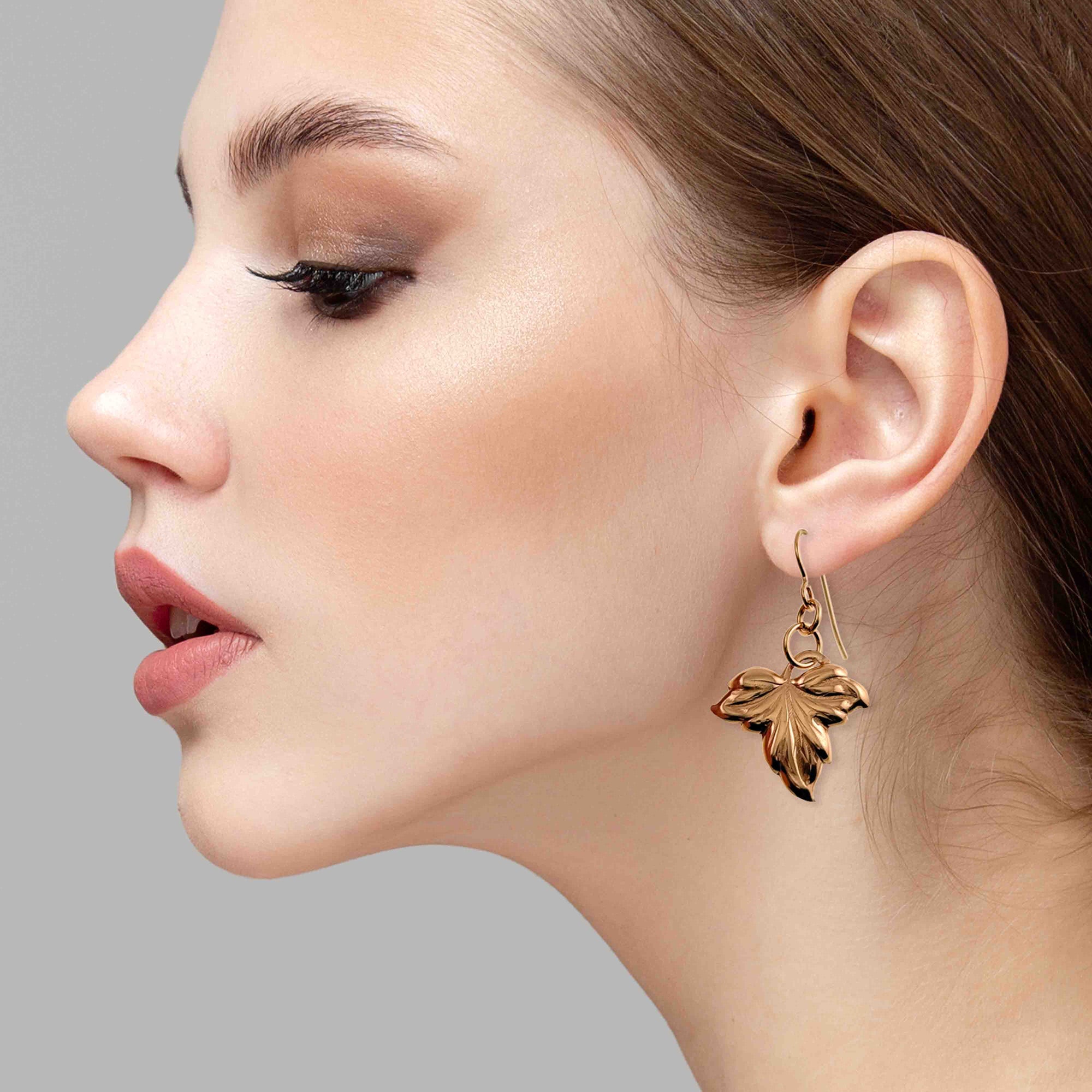 Close-up of a woman wearing a Small Maple Leaf Bronze Dangle Earring against a gray background
