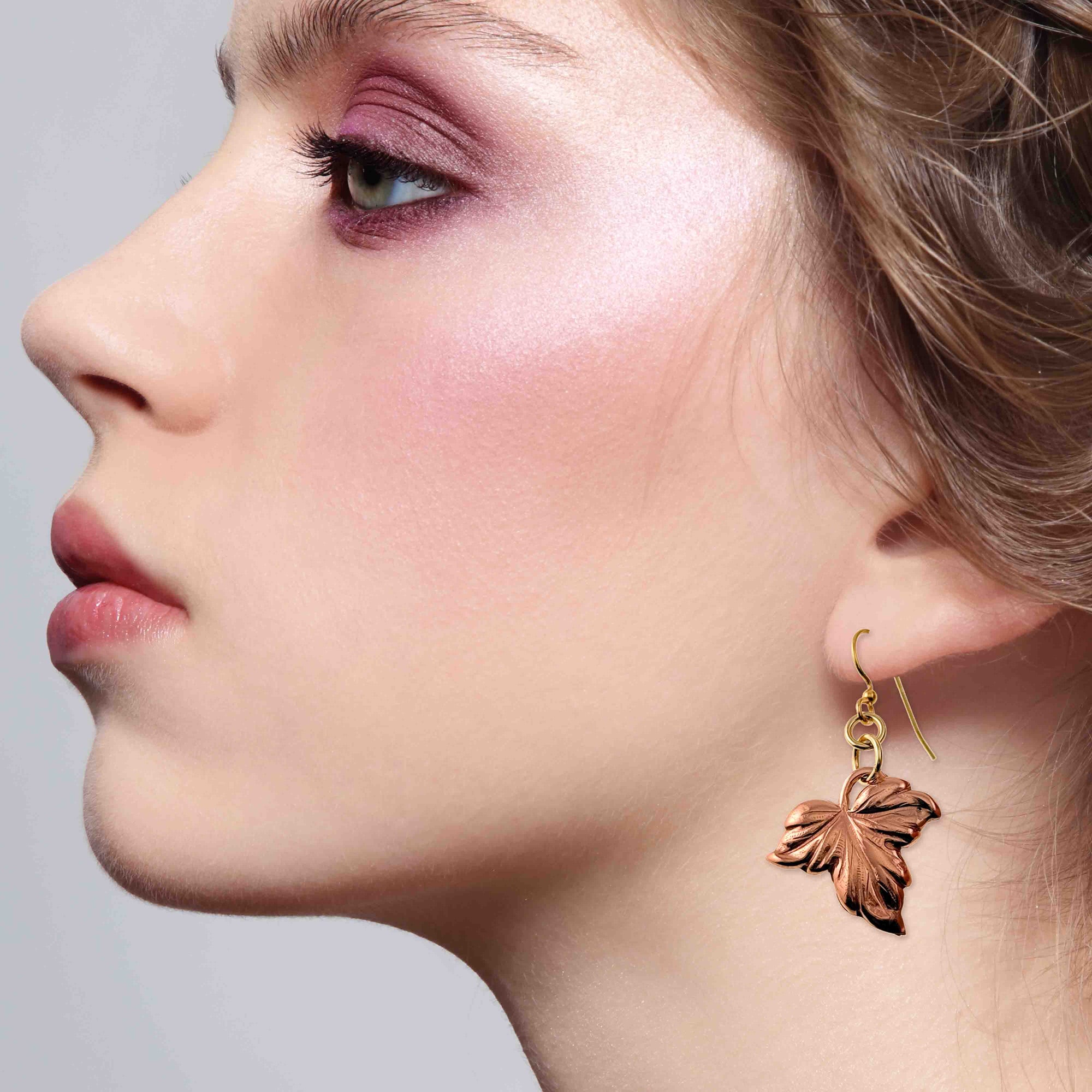 Close-up of a woman wearing a copper earring with a leaf design on a gray background