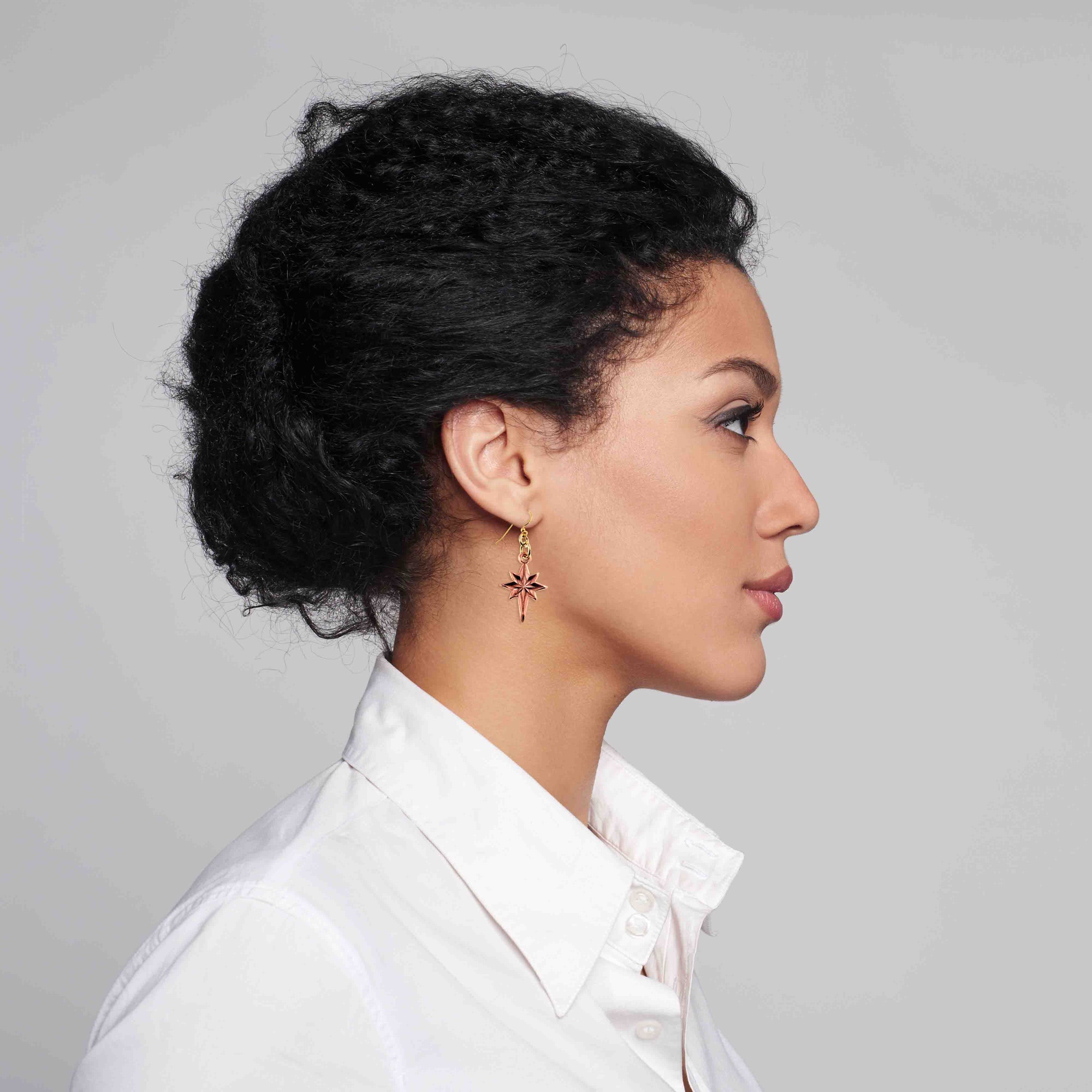 Woman with styled hair wearing a white shirt with Star of Bethlehem Copper Dangle Earrings against a gray background 