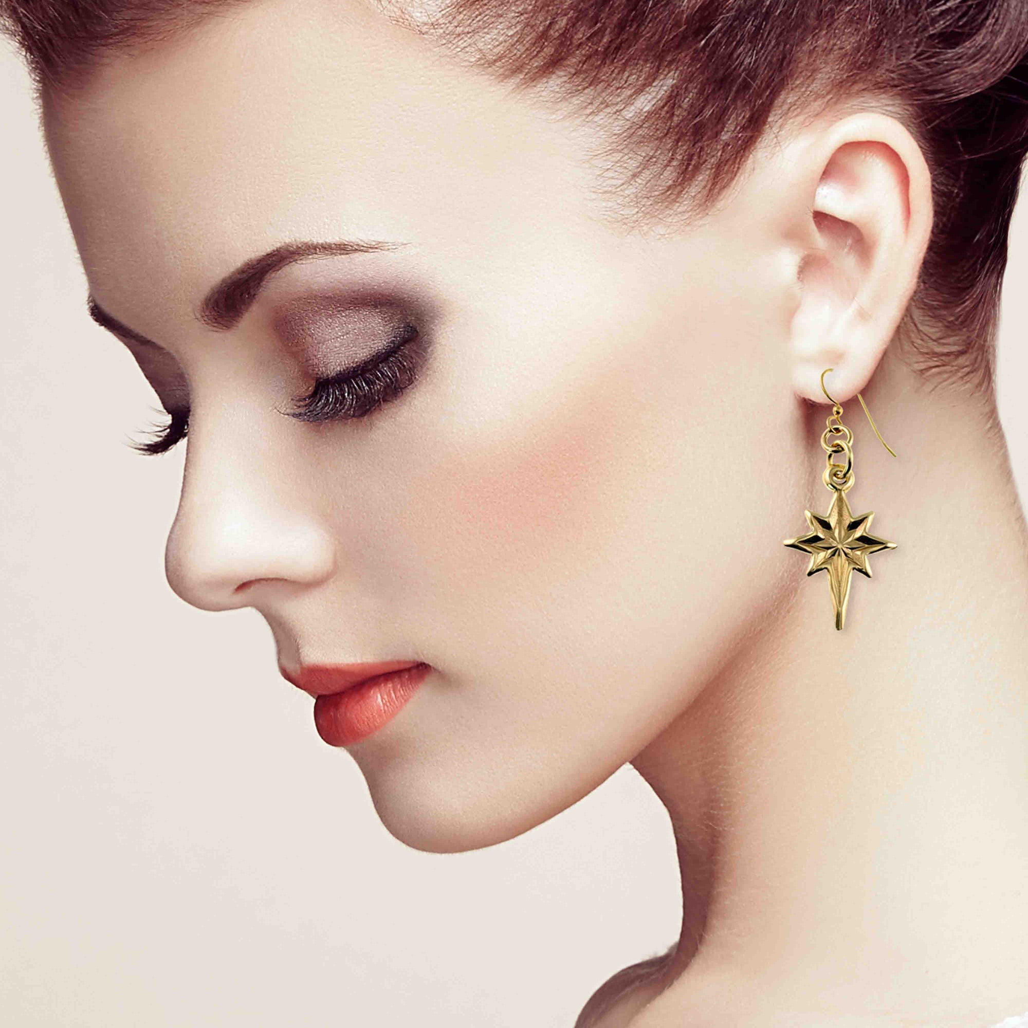 Close-up of a woman wearing Star of Bethlehem Nu Gold Brass Dangle Earrings against a neutral background