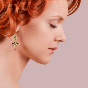 4 of 7: Profile of a woman with red hair wearing Star of Bethlehem Nu Gold Brass Dangle Earrings on a pink background