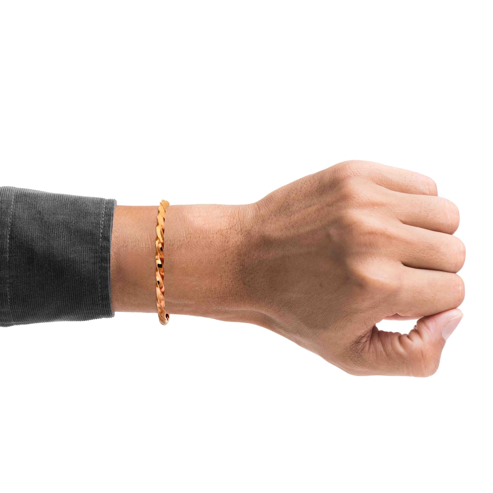 Close-up of a person wearing a slim 3mm Twisted Copper Cuff Bracelet on the wrist against a white background. The narrow open cuff features a warm polished finish and an all-over spiral twist that creates alternating highlights and shadows. A dark charcoal sleeve frames the minimalist unisex bracelet.