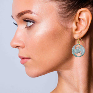 6 of 8: Female model wearing Vampire Bat Aluminum Disc Earrings in side profile portrait. Lightweight brushed aluminum disc earrings with bat cutout design hang from gold tone French ear wires. Modern gothic style jewelry paired with natural makeup and sleek pulled back hair.