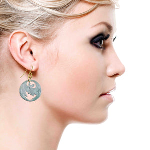 7 of 8: Blonde model wearing Vampire Bat Aluminum Disc Earrings in close side profile. Handmade brushed aluminum disc earrings feature a vampire bat silhouette design with gold tone French ear wires. Lightweight statement earrings styled with smoky eye makeup and swept back hair.
