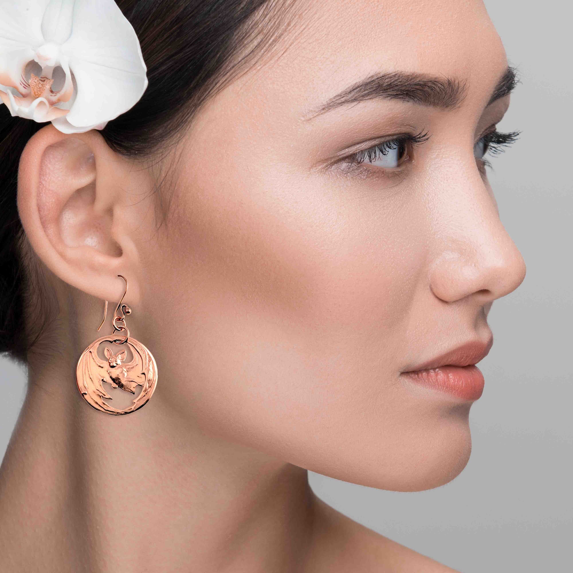 Close-up of a woman wearing Vampire Bat Copper Disc Earrings with a white orchid in her hair.