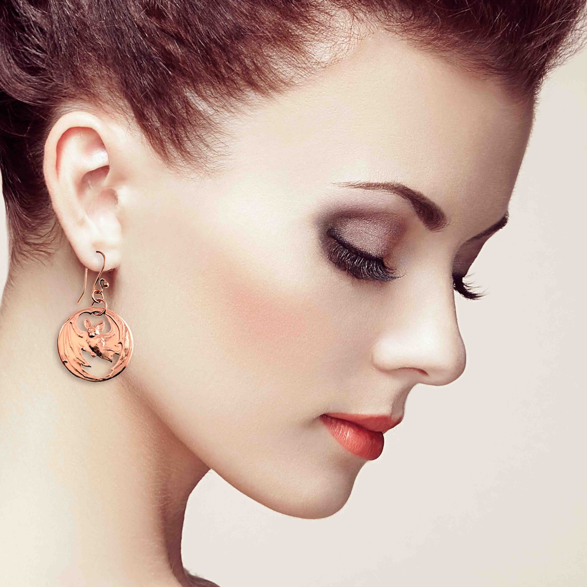 Close-up of a woman wearing Vampire Bat Copper Disc Earring on a beige background