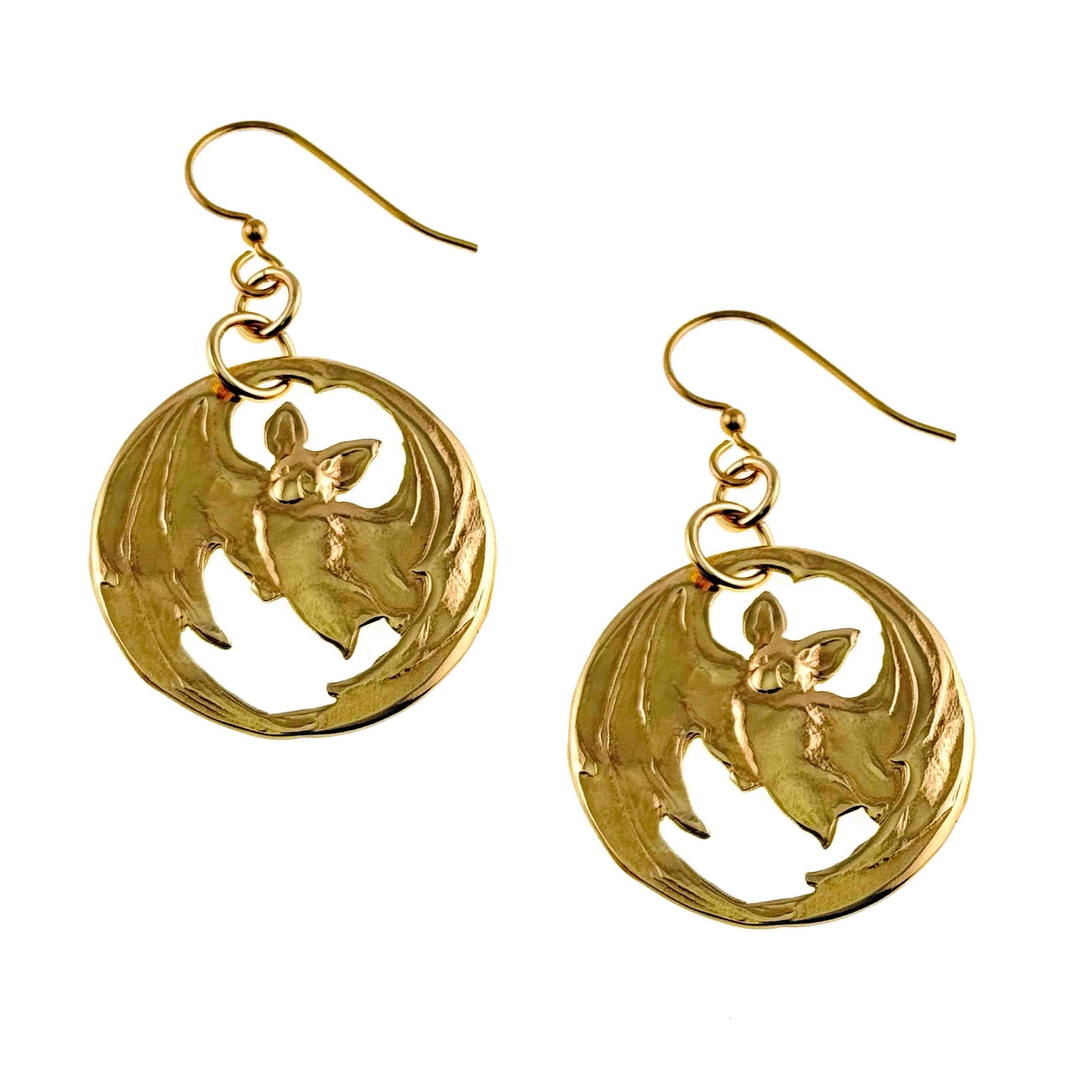 Gold-tone brass disc earrings featuring a detailed bat design with wings spread wide, created through die-struck metalwork. The bat silhouette is partially cut out, allowing light to pass through the open spaces. Each earring hangs from a brass French hook with small connecting rings, offering gentle movement and a warm polished finish.