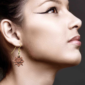 6 of 7: Close-up of a woman wearing a Victorian Copper Snowflake Dangle Earring with a dark background