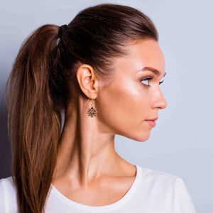 2 of 7: Woman with a ponytail wearing Victorian Copper Snowflake Dangle Earrings against a gray background