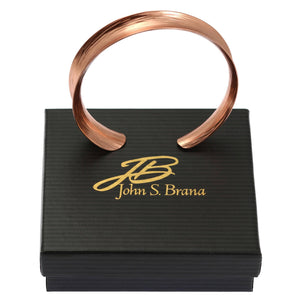7 of 7: Anticlastic Bark Copper Bangle Bracelet on top of a Black Gift Box with Gold Logo