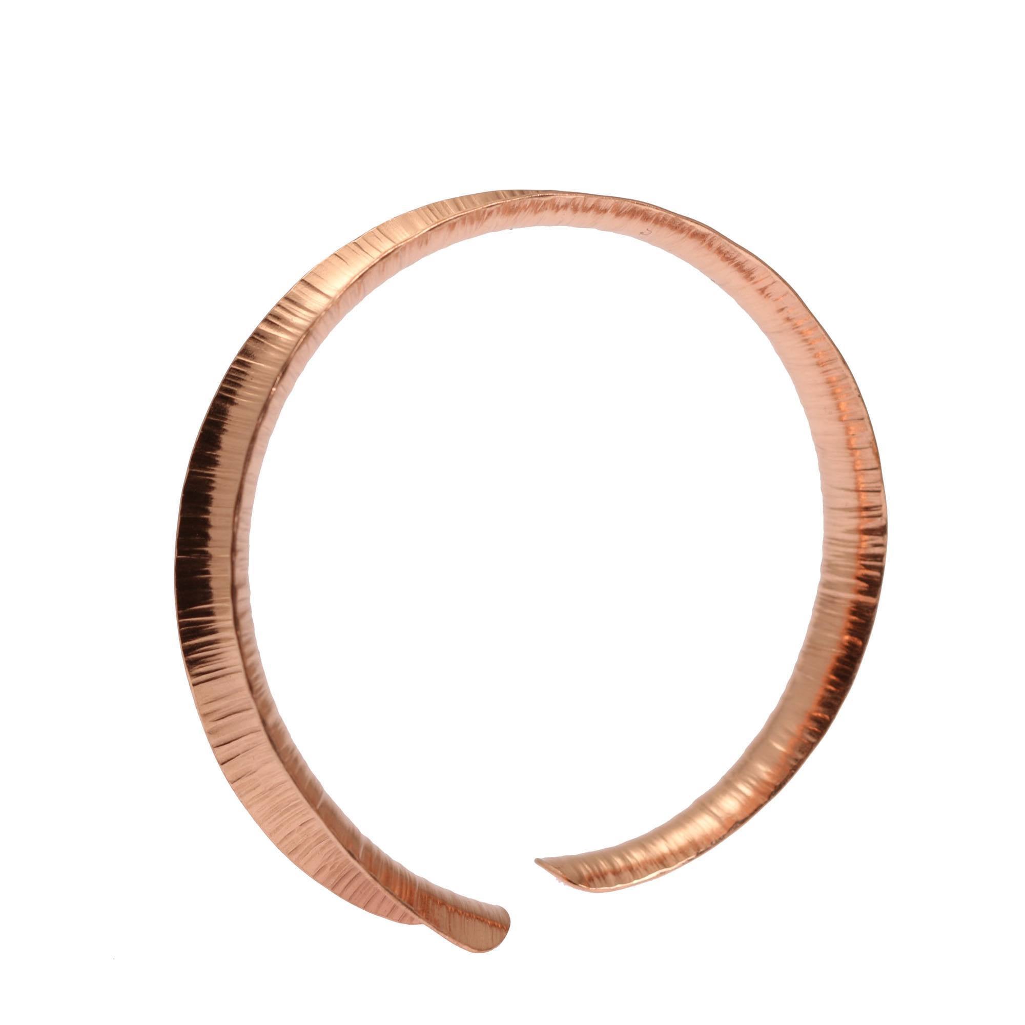 A handcrafted copper cuff bracelet with a chased texture and a warm, reddish-gold finish. The bracelet has a slim, slightly tapered design with an open end, making it easy to adjust for a comfortable fit. The surface features fine, vertical hammer marks that catch the light, giving it a subtle shimmer and artisanal feel. Its clean, minimalist shape makes it versatile for both casual and dressy outfits. Photographed against a plain white background.
