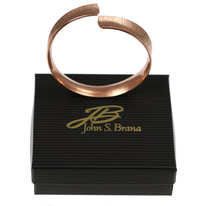 6 of 6: Chased Copper Bangle Bracelet on top of a Black Gift Box with Gold Logo