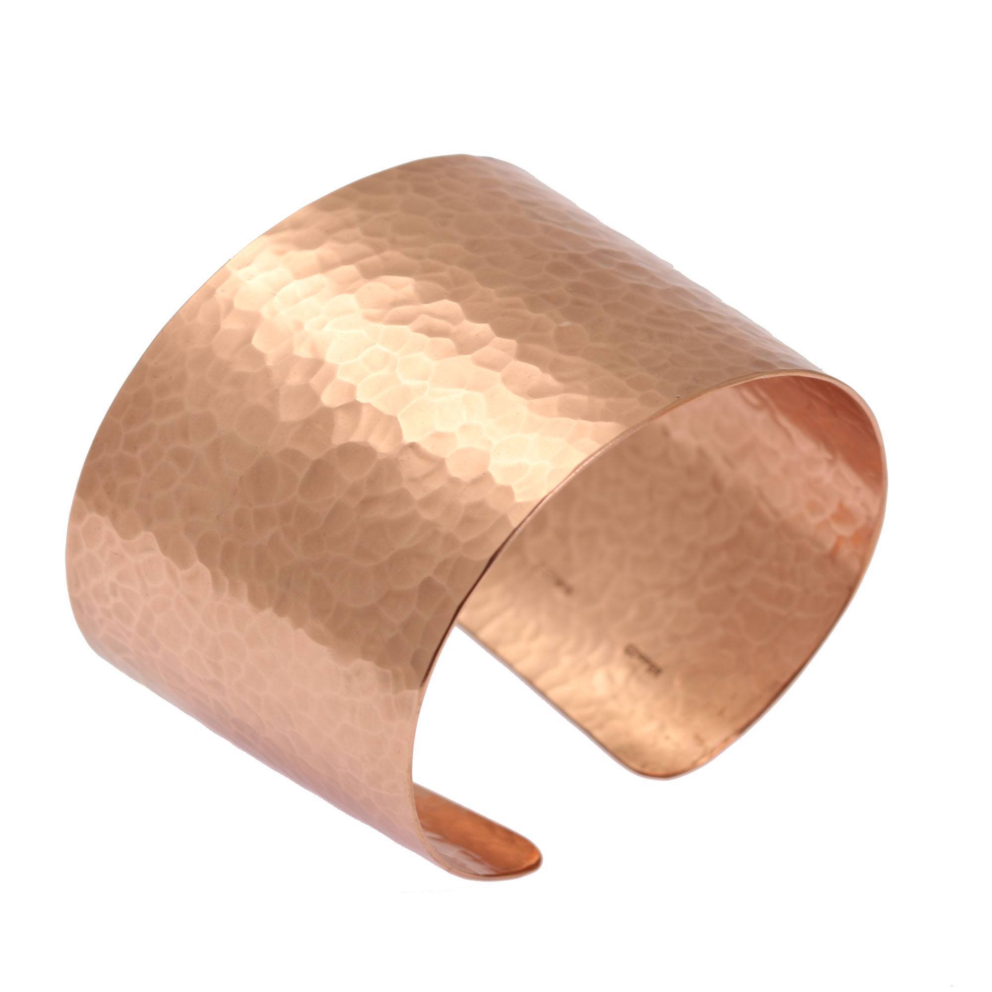 Wide hammered copper cuff bracelet with a warm polished finish, photographed at an angle on a white background. The open cuff features a broad curved band, softly rounded edges, and an all-over hand-hammered texture that catches the light. The interior shows subtle artisan markings near the opening.