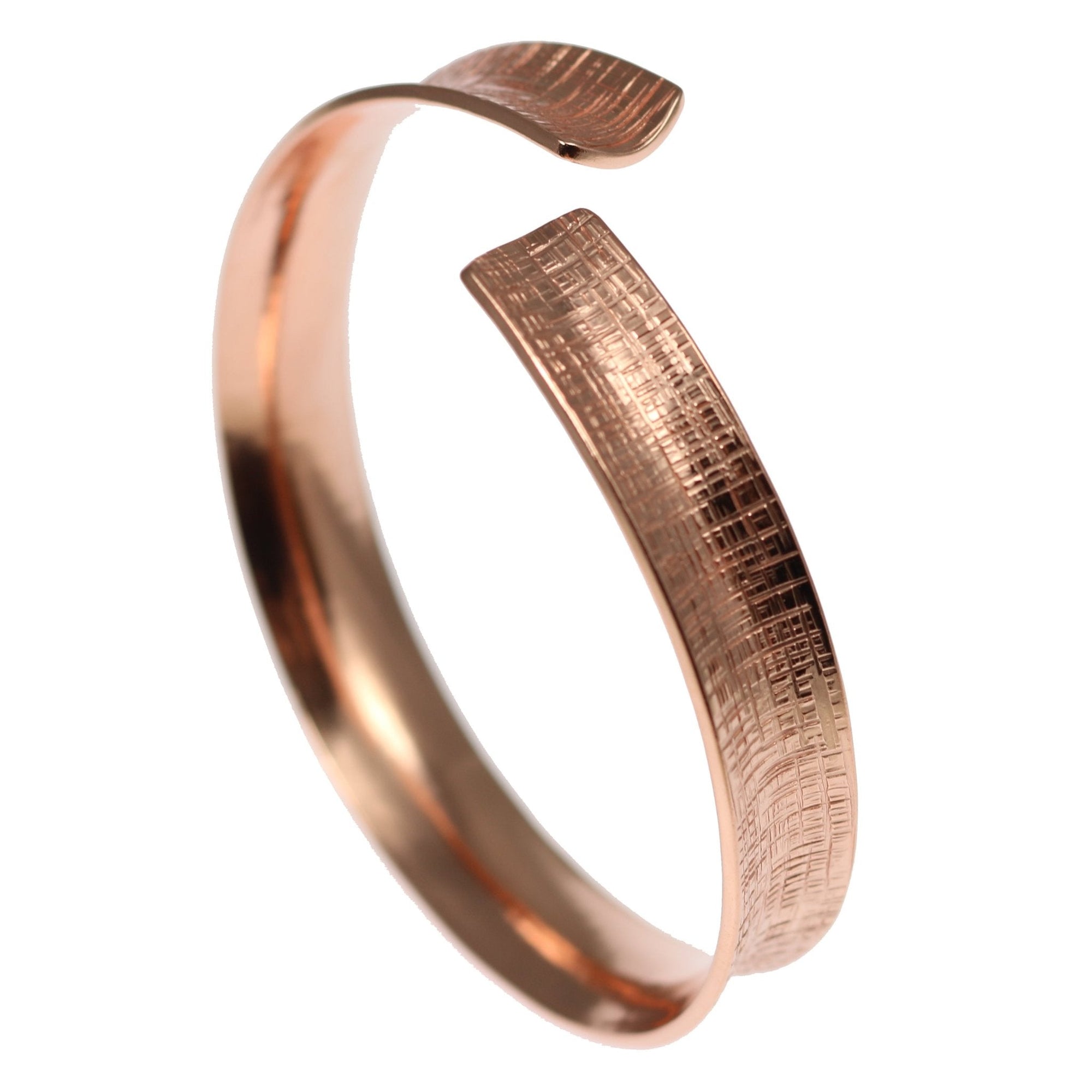 Anticlastic copper bangle bracelet shown against a white background, photographed at an angle to highlight its curved, open-ended form and sculptural profile. The solid copper bracelet features a smooth polished interior and a finely textured exterior with a subtle linen-like crosshatch pattern that follows the contour of the band. The warm copper tone and gently flared edges emphasize the bracelet’s handcrafted design, giving it a refined, modern look with dimensional depth and comfortable wearability.