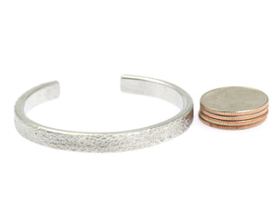 6 of 7: Width of Thin Texturized Aluminum Cuff Bracelet compared to a stack of 4 US Quarter Coins